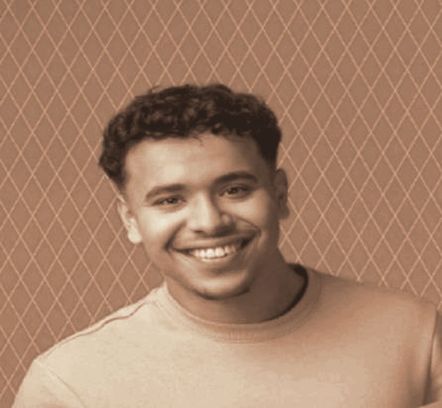 Youssef El Boujeddaini smiling, in a light sweater, in warm tones